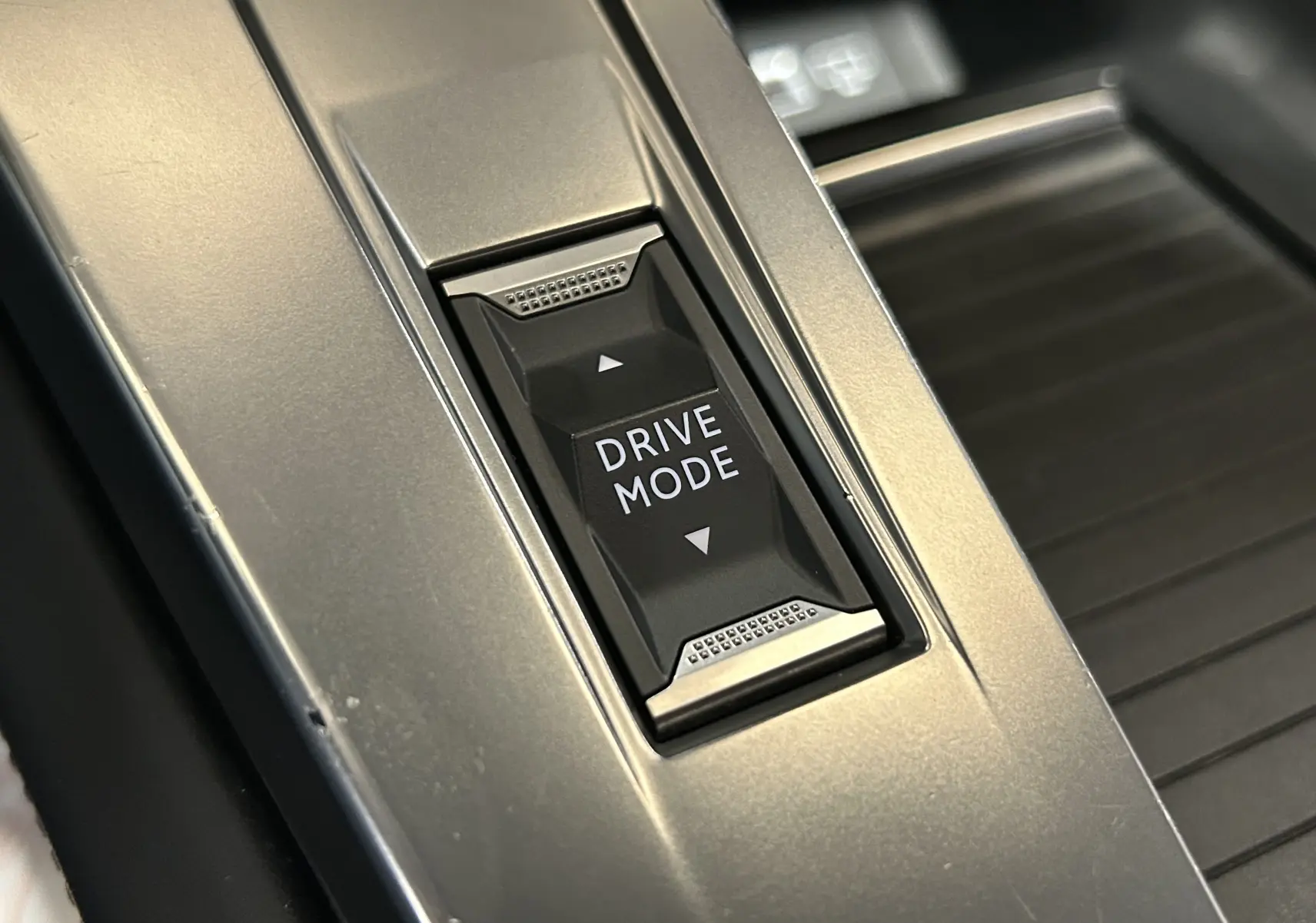 Gros plan sur le bouton Drive Mode noir encadré d'inox brossé dans la console centrale de la Peugeot 308 gris 2022.