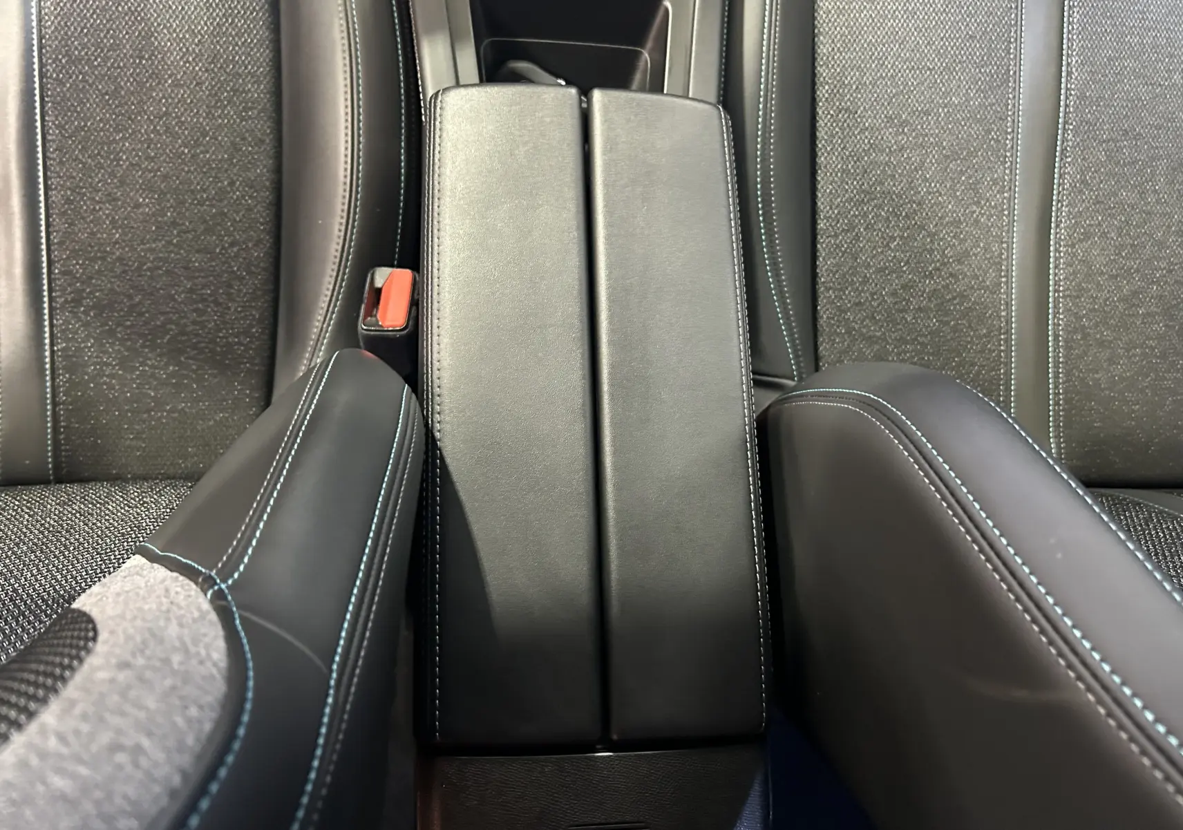 Gros plan sur l'accoudoir central en cuir noir avec surpiqûres bleues, entre les sièges arrière gris tissu de la Peugeot 308.