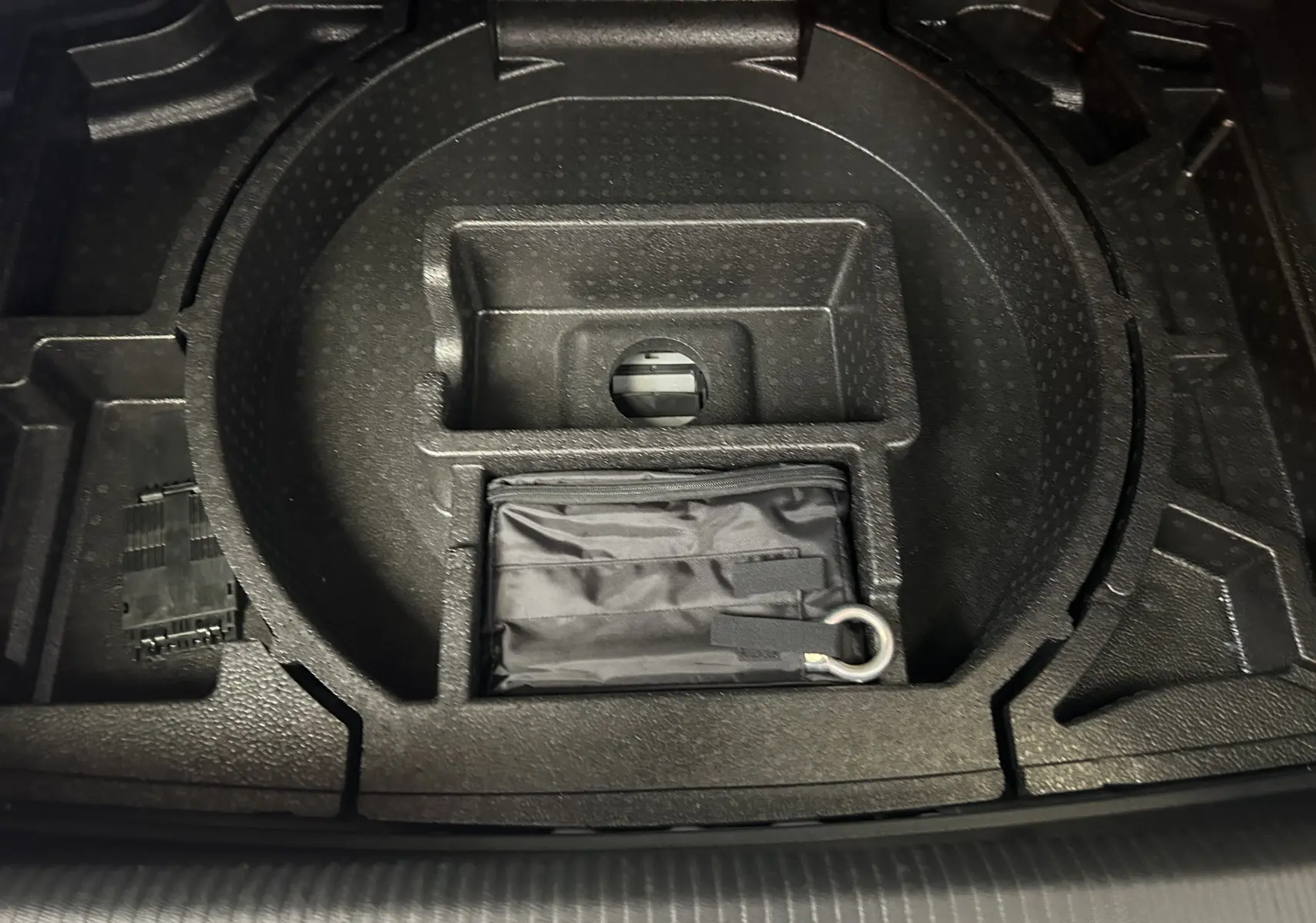 Rangement sous coffre de la Peugeot 308 gris 2022, montrant un compartiment circulaire avec un kit de secours noir.