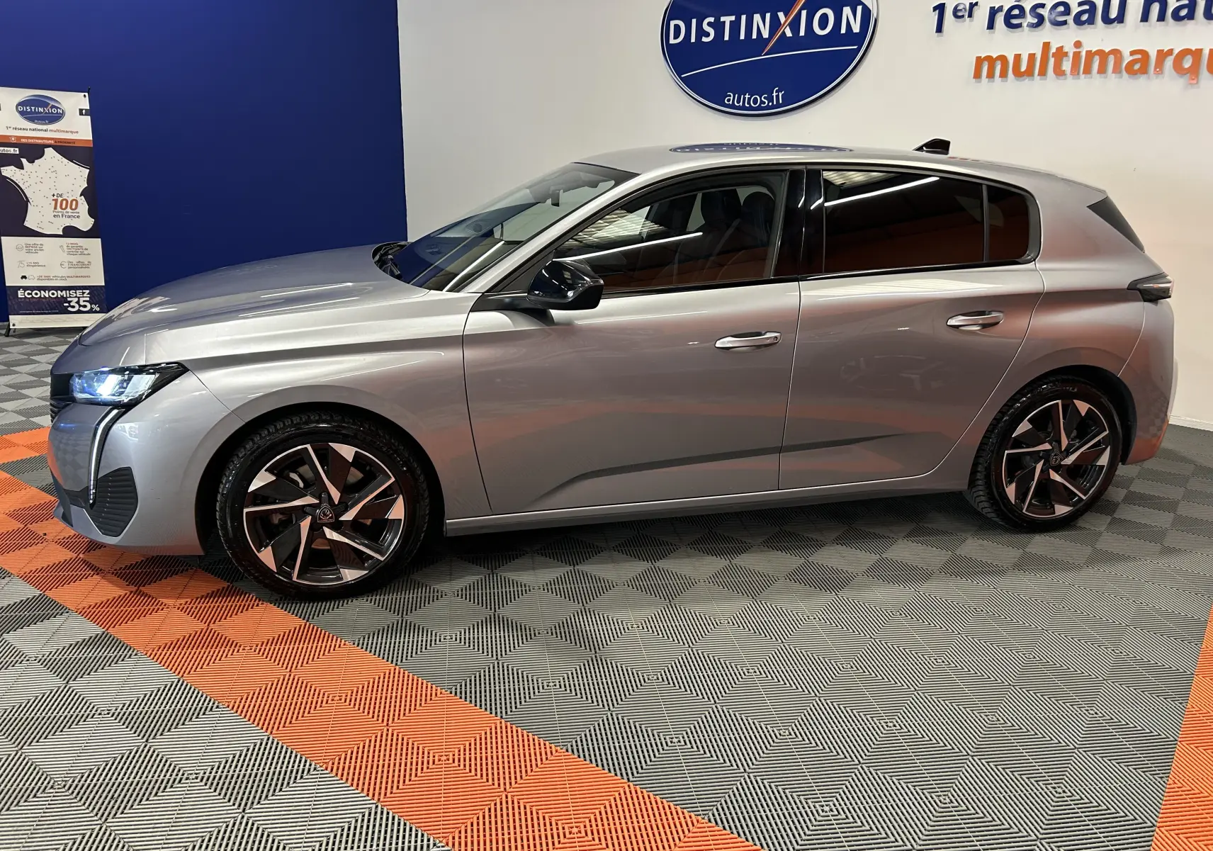 Profil droit d’une Peugeot 308 gris métallisé 2022 dans un showroom avec jantes alliage et phares allumés.