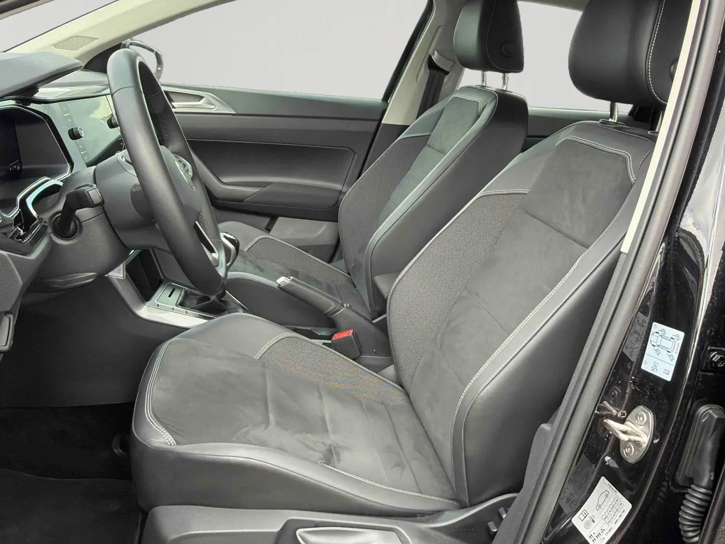 Vue intérieure côté conducteur de la Volkswagen Polo noire 2025, sièges en cuir et alcantara avec coutures contrastées.