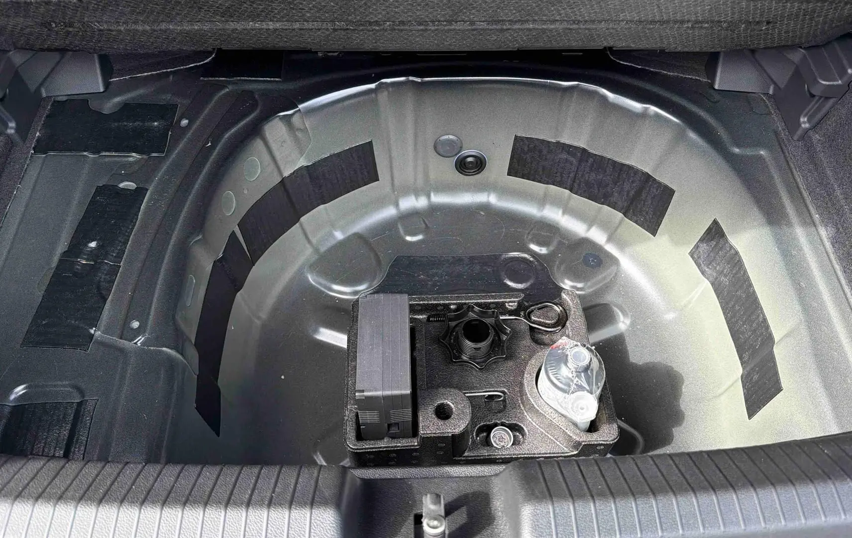 Coffre ouvert vu de dessus montrant le rangement sous plancher avec kit de dépannage sur Volkswagen Polo noire 2025.