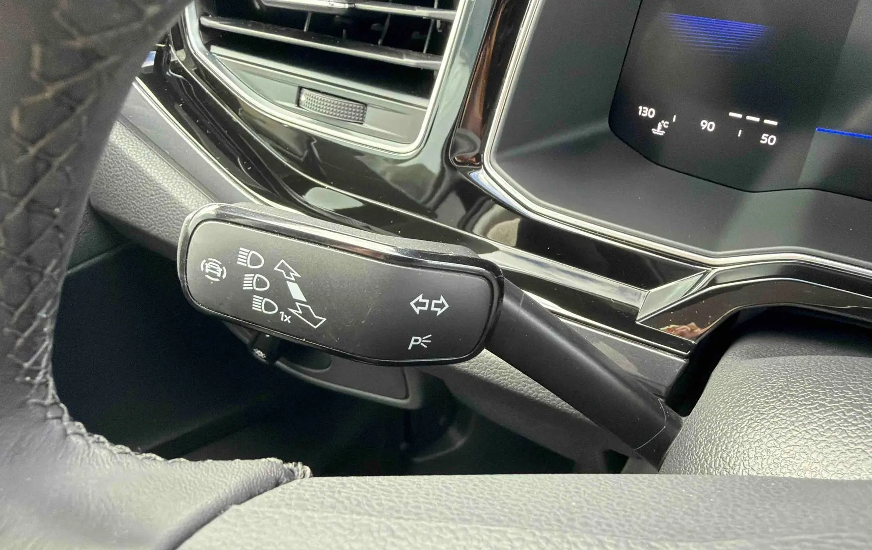 Gros plan sur le commodo de clignotants noir à gauche du volant dans l’habitacle d’une Volkswagen Polo noire.