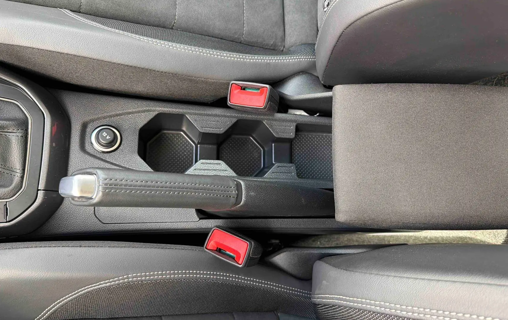Vue plongeante sur la console centrale noire de la Volkswagen Polo 2025, avec frein à main manuel et porte-gobelets.