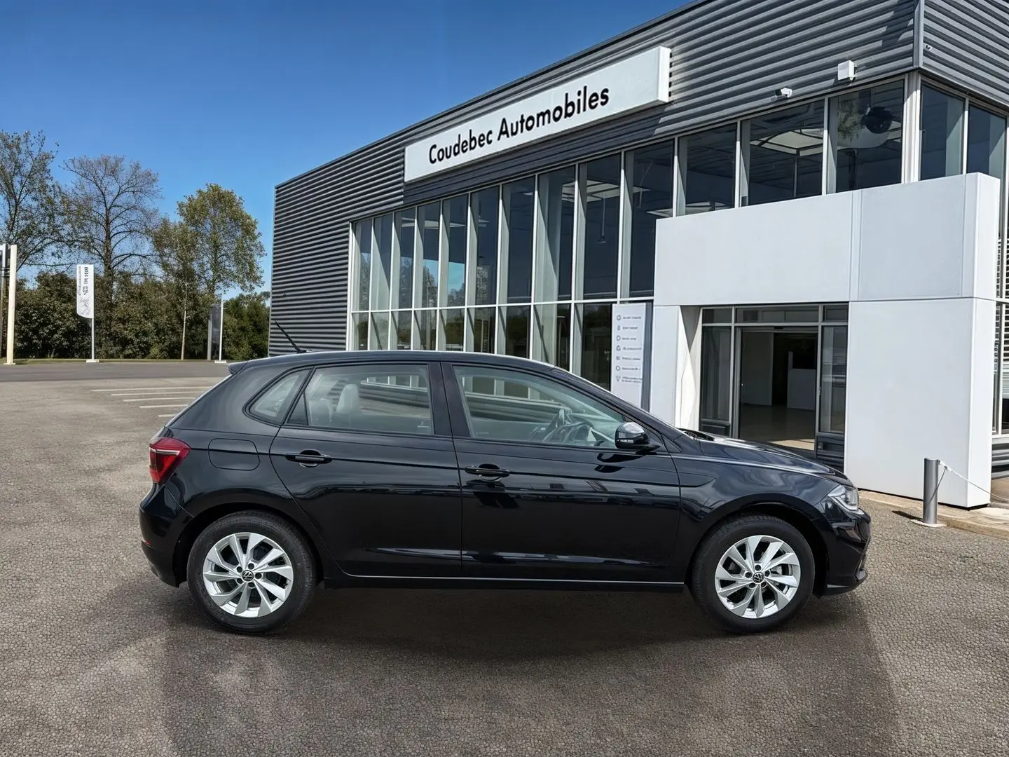 Profil latéral droit d'une Volkswagen Polo noire 2025 stationnée devant un bâtiment vitré de concession.