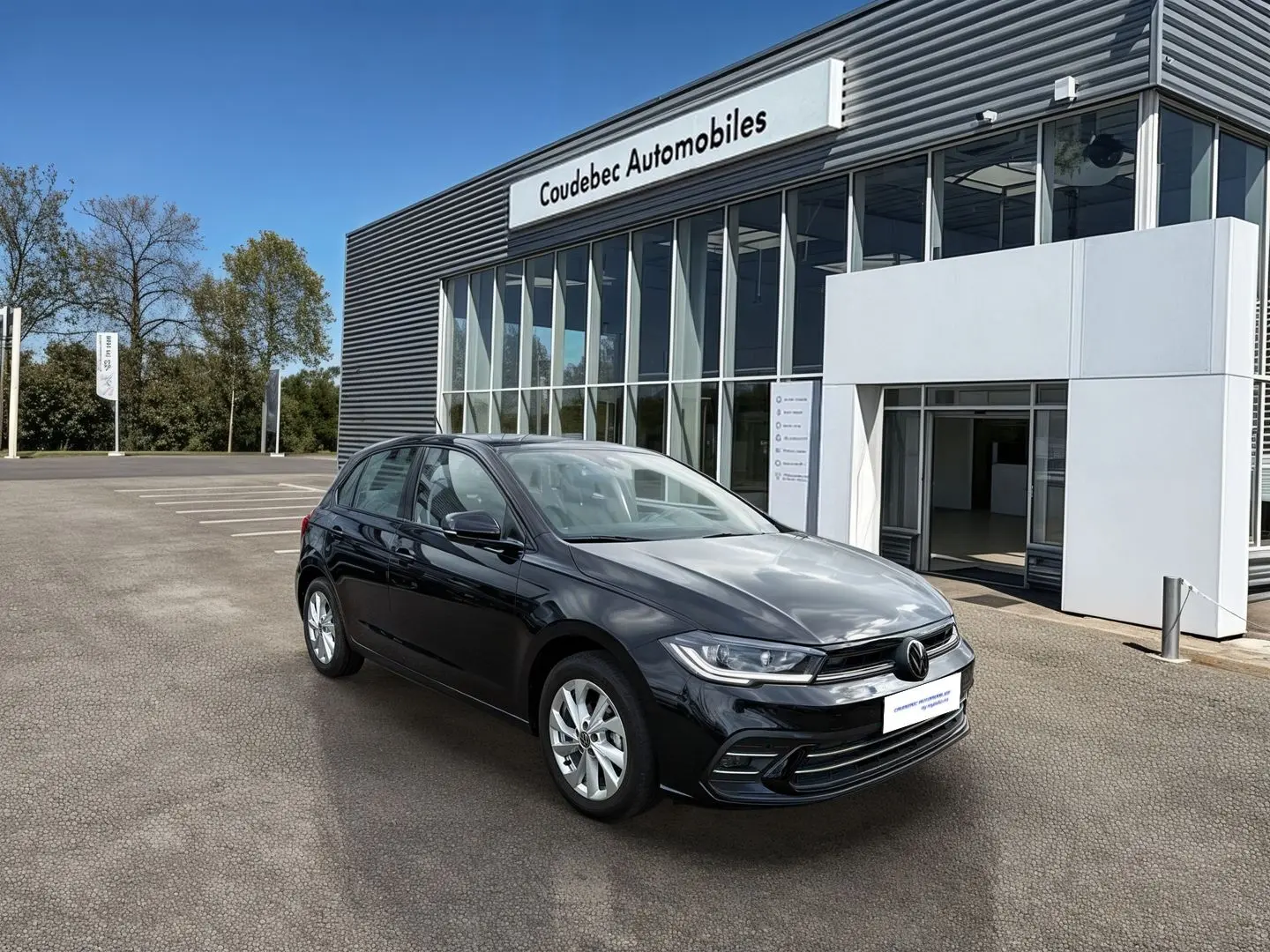 Volkswagen Polo noire vue en 3/4 avant droit devant un bâtiment moderne de concession automobile.