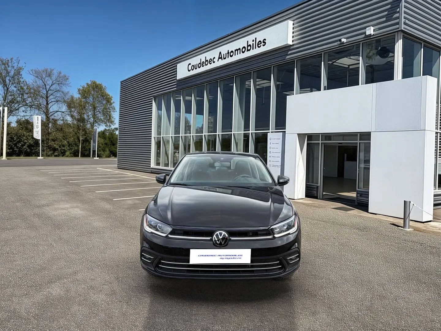 Vue avant d'une Volkswagen Polo noire 2025 stationnée devant un bâtiment moderne de concession automobile.