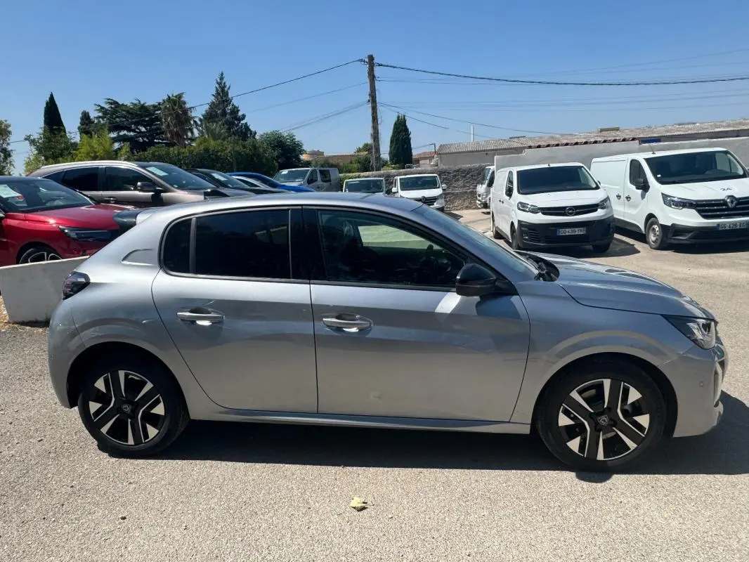 Profil côté gauche d'une Peugeot 208 Hybrid 110 gris métallisé avec jantes alliage 16 pouces, en extérieur parking.