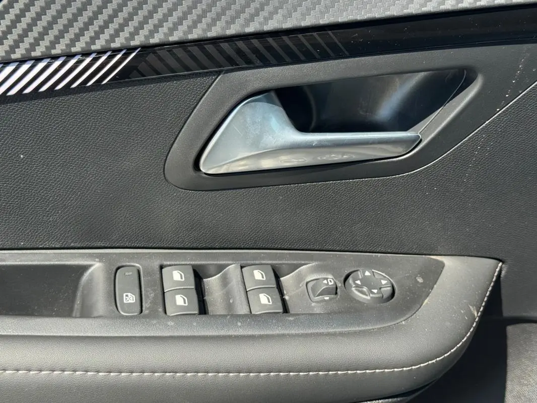 Gros plan sur la poignée intérieure et les commandes des vitres électriques côté conducteur d’une Peugeot 208 gris 2025.