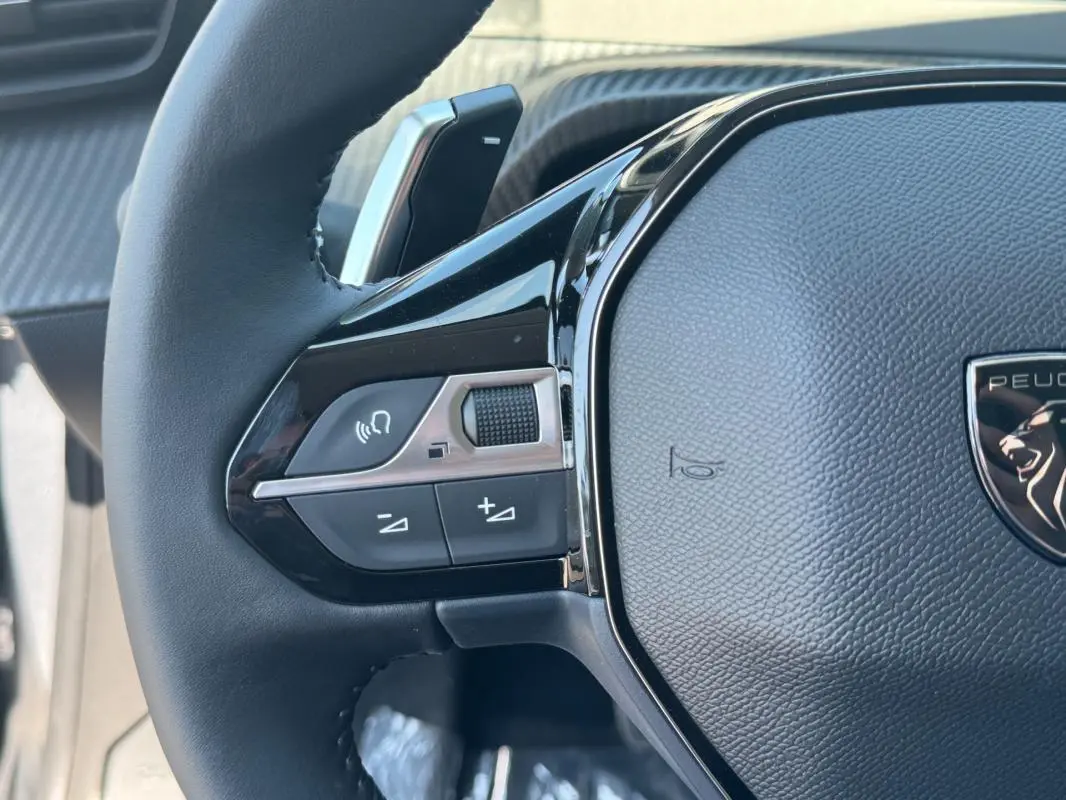Gros plan sur le volant noir de la Peugeot 208 Hybrid 110 e-DCS6 Allure avec commandes intégrées côté gauche.