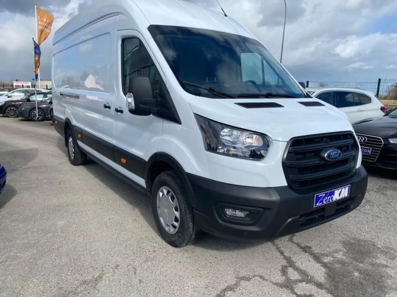 Ford Transit Fourgon blanc vu en 3/4 avant droit, avec calandre noire et pare-chocs noir mat, stationné en extérieur.