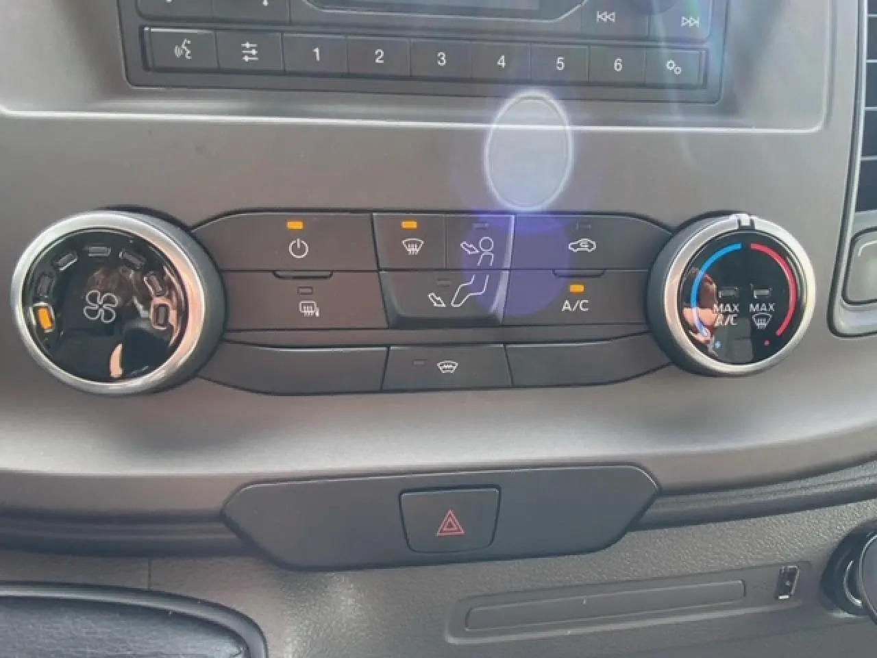 Gros plan sur les commandes de climatisation manuelle du Ford Transit Fourgon blanc 2023 avec boutons éclairés.