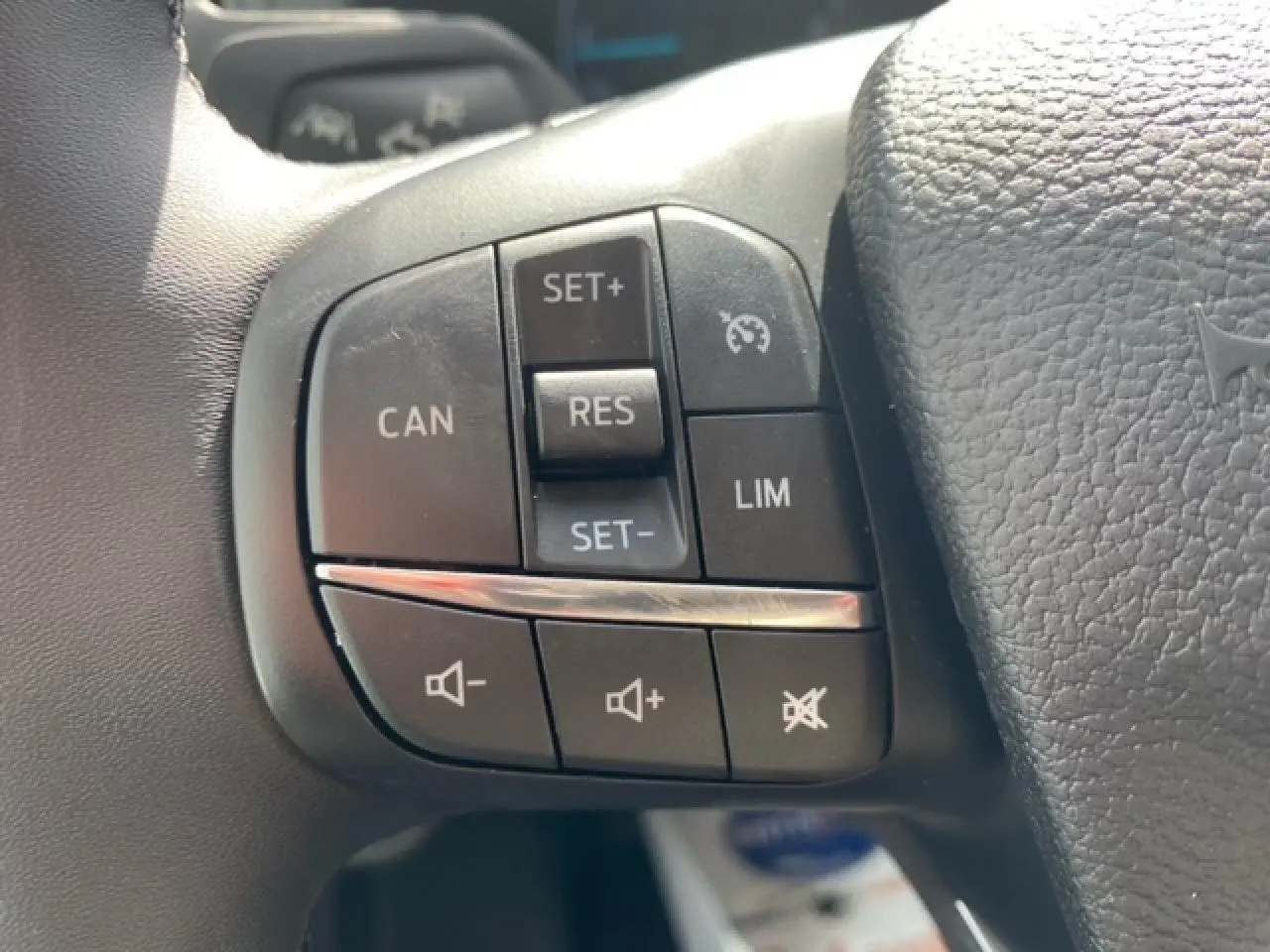 Gros plan sur les commandes du régulateur de vitesse et du volume audio sur le volant noir du Ford Transit Fourgon blanc 2023.