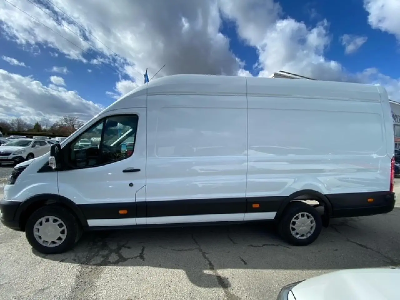 Fourgon Ford Transit blanc en vue profil côté gauche, avec porte latérale coulissante et jantes acier.