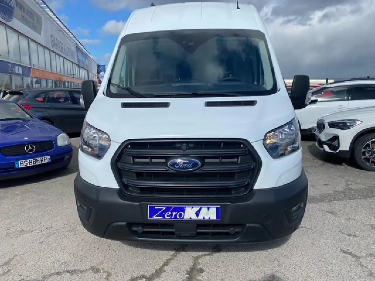 Vue frontale d'un Ford Transit Fourgon blanc 2023 avec calandre noire et plaque "Zéro KM" visible.