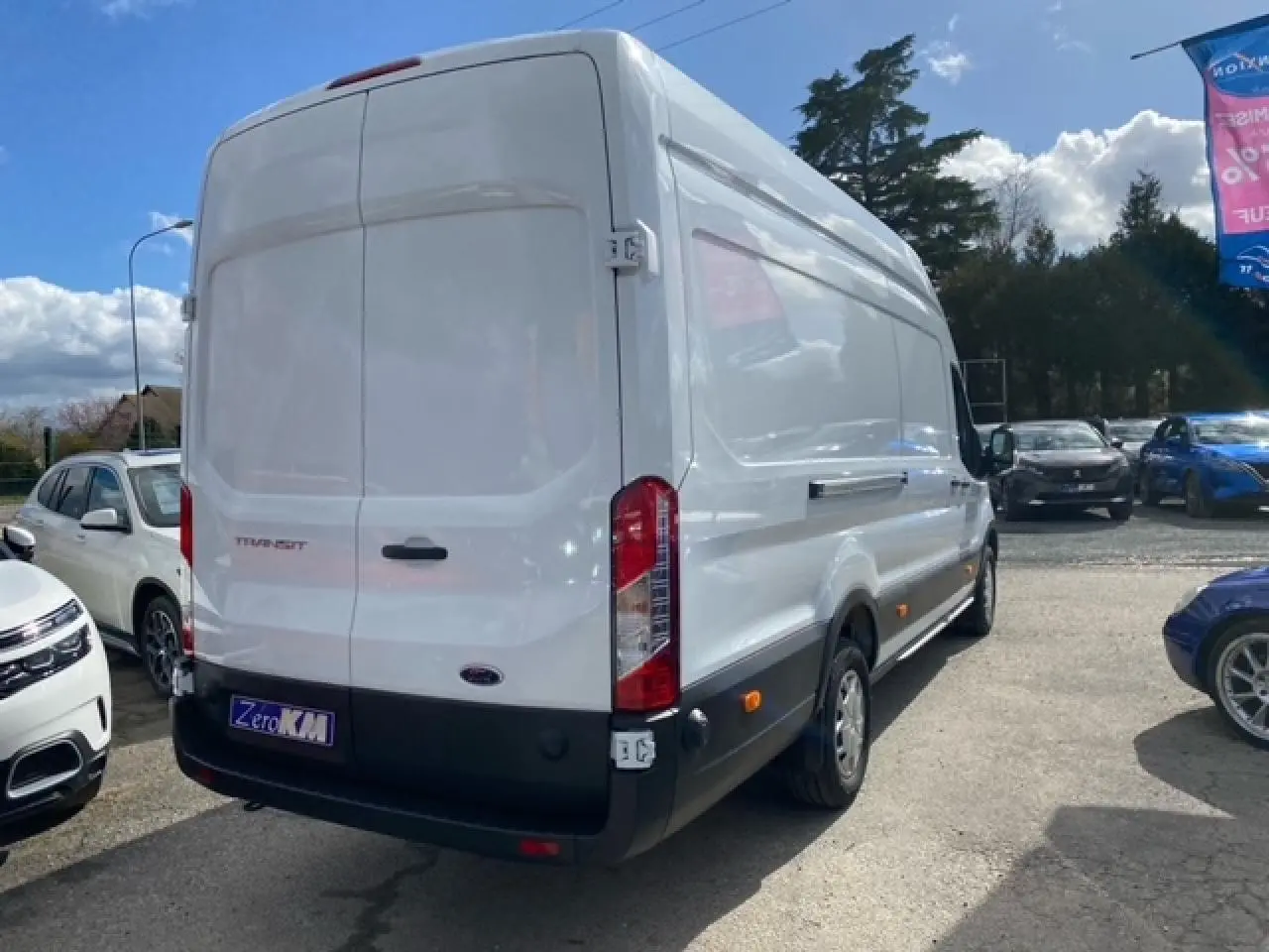 Vue 3/4 arrière droite d'un fourgon Ford Transit blanc 2023 avec porte latérale coulissante et feux arrière verticaux.