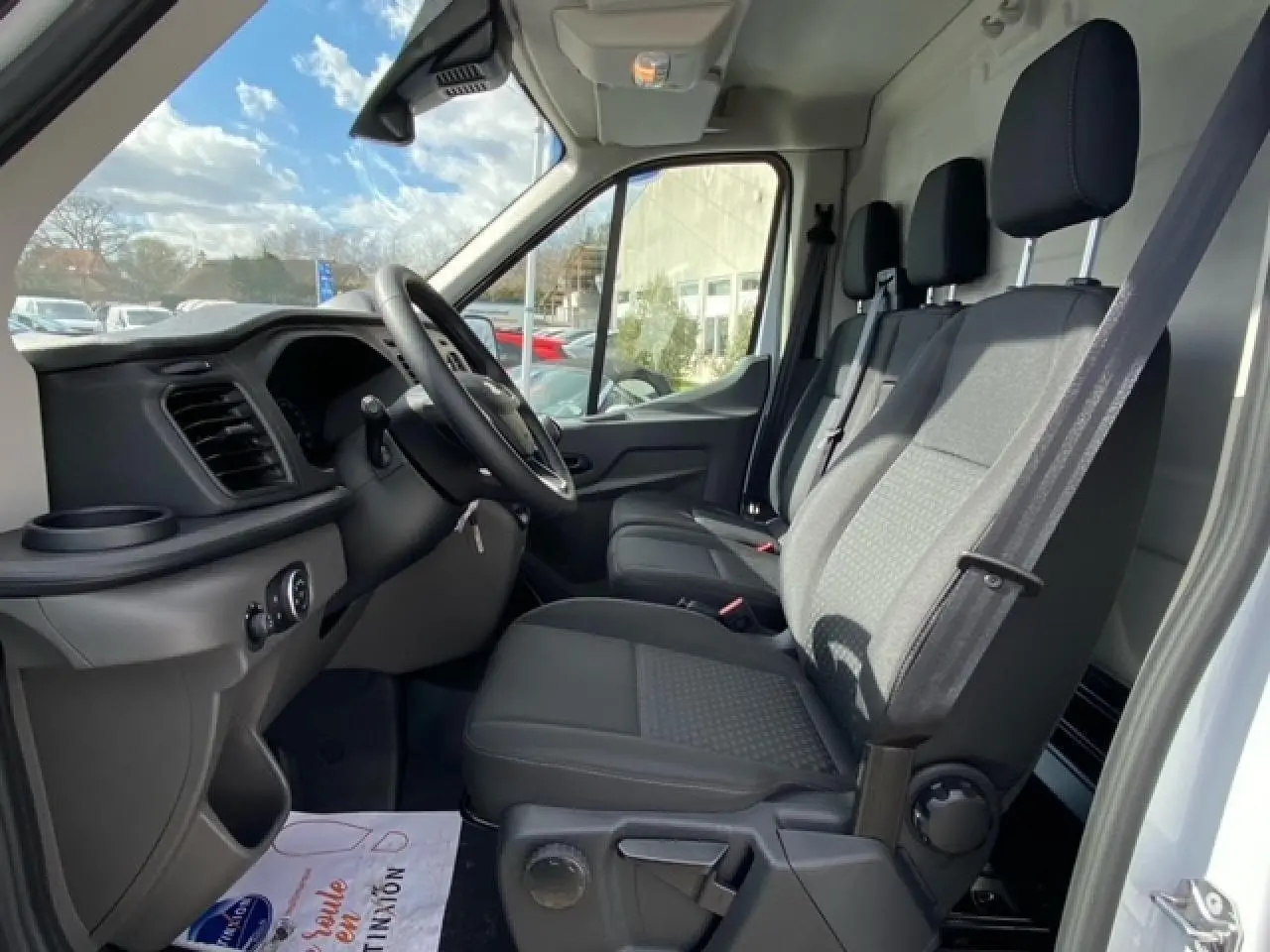 Vue intérieure côté conducteur du Ford Transit Fourgon blanc 2023, montrant les sièges avant et le tableau de bord noir.