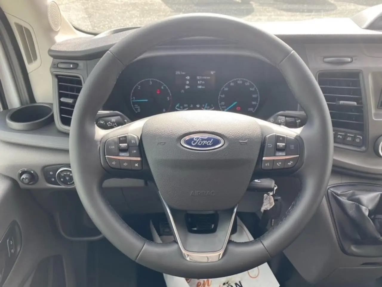 Vue rapprochée du volant multifonction du Ford Transit Fourgon 2023 avec tableau de bord et levier de vitesses visibles.