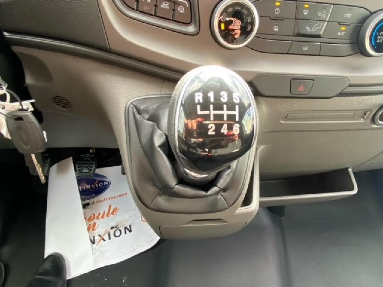 Le levier de vitesses manuel noir du Ford Transit Fourgon 2023, avec tableau de bord gris en arrière-plan.