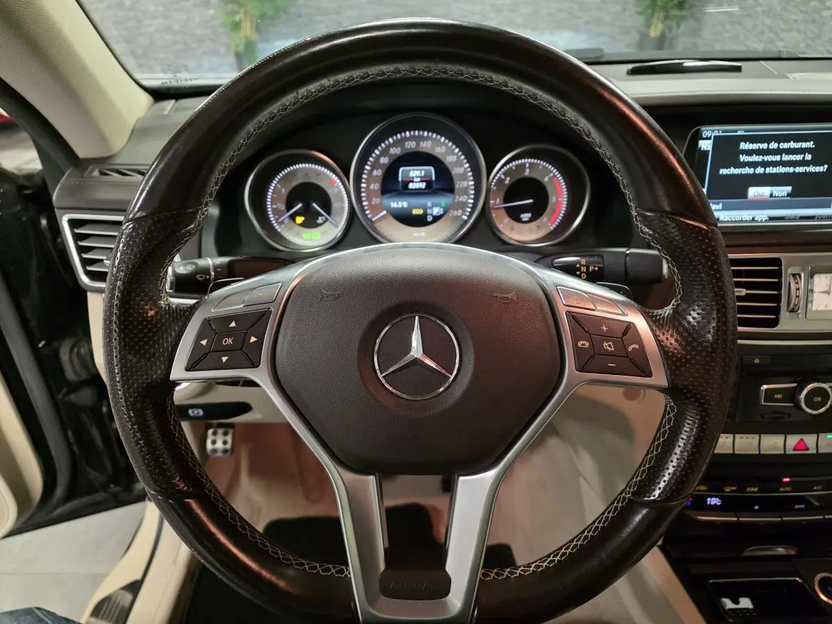 Vue rapprochée du volant en cuir noir perforé de la Mercedes Classe E Cabriolet 2014 avec tableau de bord et écran multimédia.