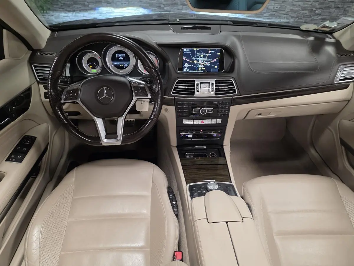 Vue intérieure avant de la Mercedes Classe E Cabriolet 2014 avec tableau de bord noir et sièges en cuir beige.