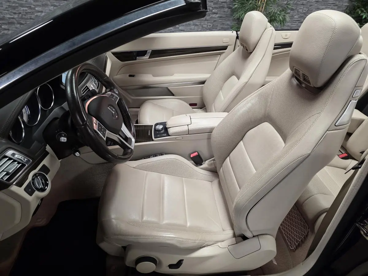 Intérieur beige clair d'une Mercedes Classe E Cabriolet 2014, vue côté conducteur avec sièges en cuir et volant multifonctions.