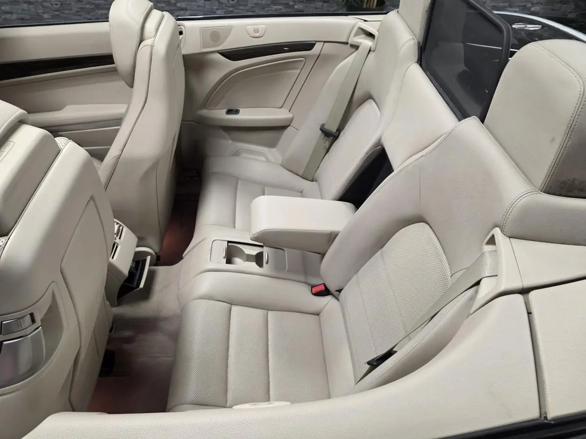Vue intérieure arrière côté droit d'un cabriolet Mercedes Classe E 250 CDI noir avec sièges en cuir beige et accoudoir central relevé.