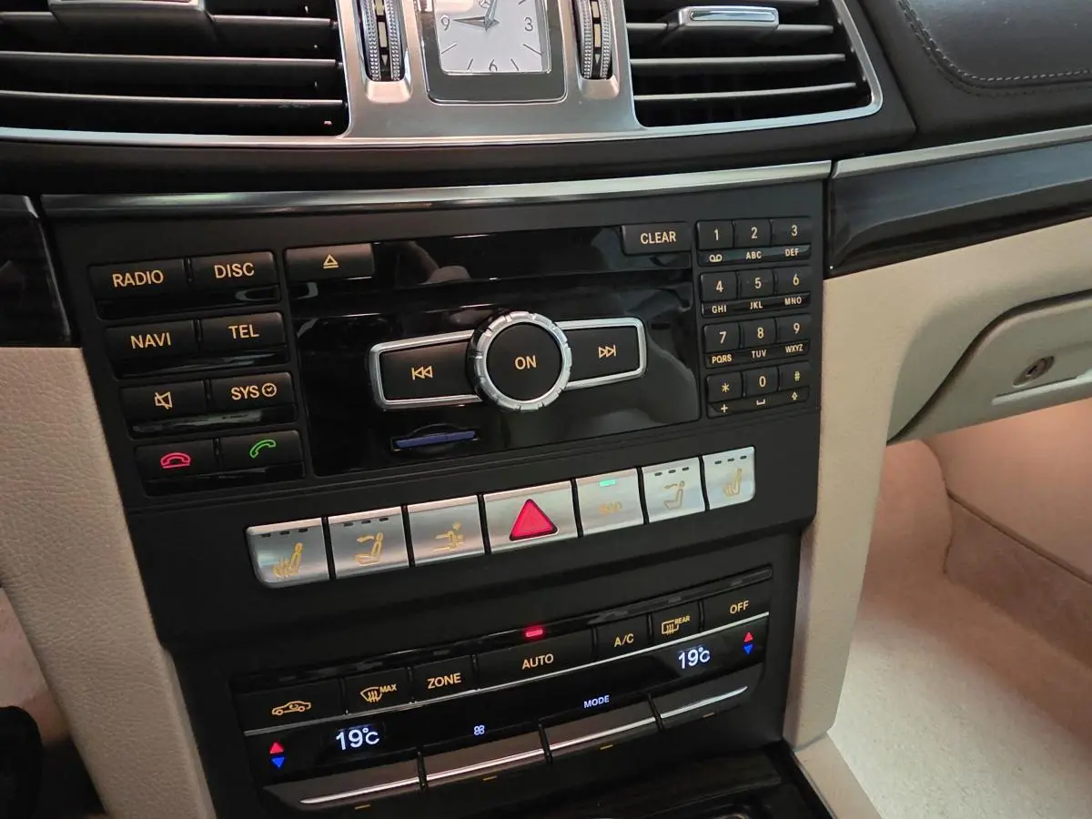 Console centrale beige et noire de la Mercedes Classe E Cabriolet 2014 avec commandes multimédia et climatisation automatique affichant 19°C