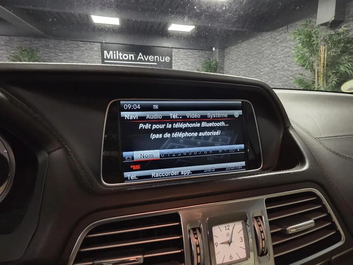 Vue intérieure du tableau de bord cuir noir de la Mercedes Classe E Cabriolet avec écran multimédia et horloge analogique centrale.