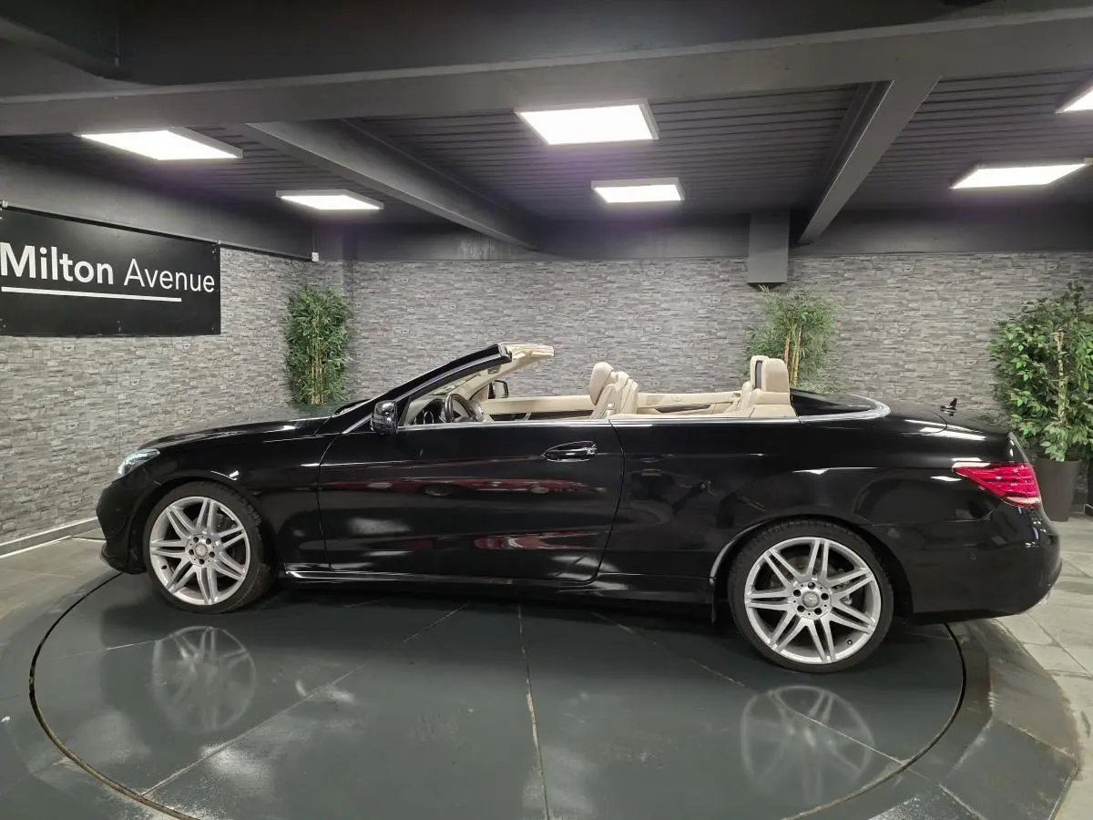 Profil droit d'une Mercedes Classe E Cabriolet noire avec intérieur cuir beige et jantes AMG 19 pouces en showroom.