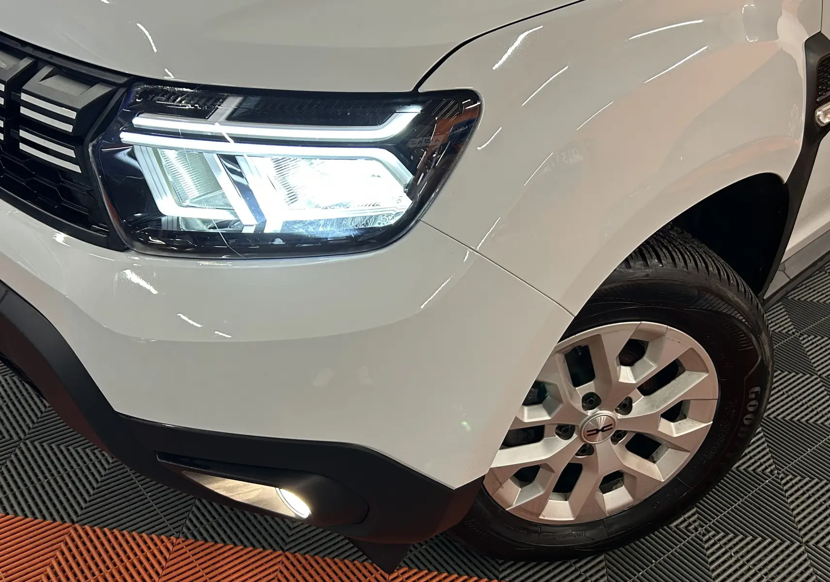 Gros plan sur l'avant droit blanc du Dacia Duster 2024, mettant en valeur le phare LED et la roue en alliage.