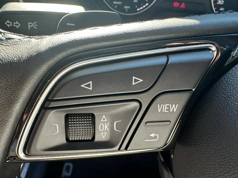 Gros plan sur les commandes multifonctions à gauche du volant d’un Audi Q2 blanc 2023, finition S line.