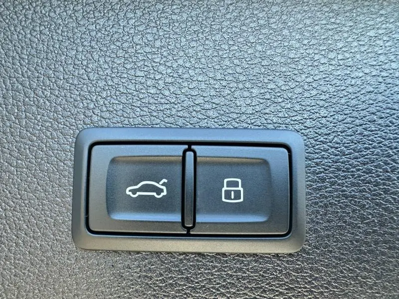 Gros plan sur les boutons d'ouverture du coffre et de verrouillage dans l'Audi Q2 blanc 2023, intérieur noir texturé.