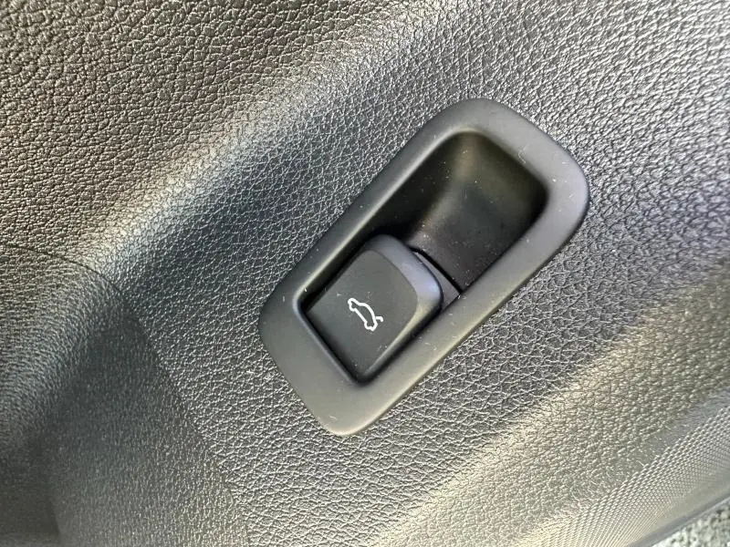 Bouton d'ouverture du coffre noir intégré dans la garniture intérieure texturée d'un Audi Q2 blanc 2023.