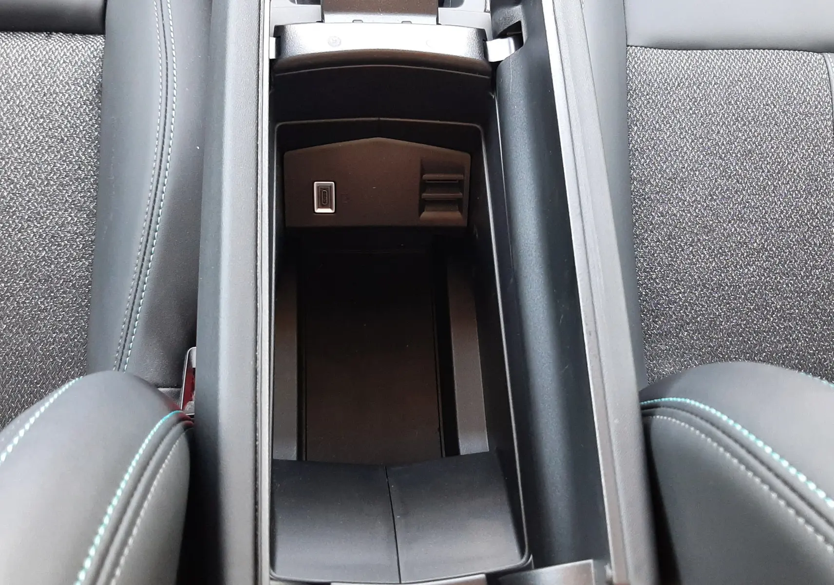 Vue plongeante sur le rangement central ouvert de la Peugeot 408 gris selenium, montrant un port USB et sellerie tissu et cuir noir.