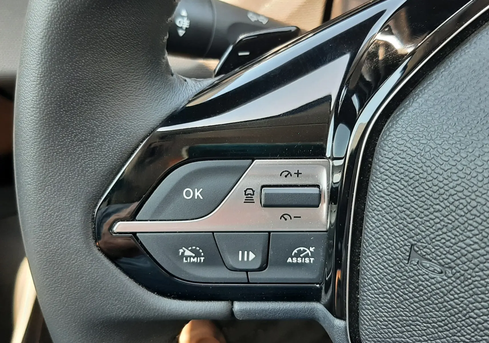 Gros plan sur les commandes gauche du volant noir du Peugeot 408 Hybrid 145ch 2024, boutons de régulateur et assistant.