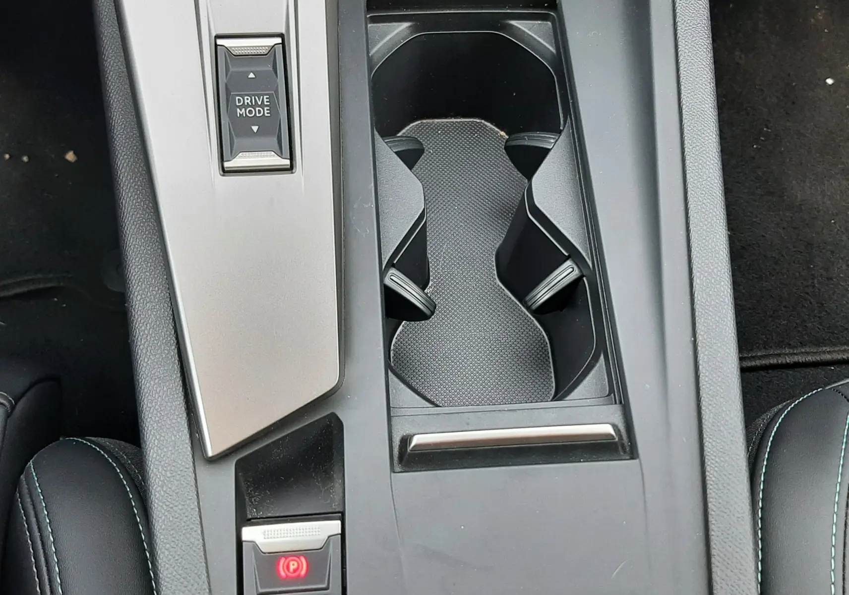 Vue plongeante sur la console centrale noire de la Peugeot 408 Hybrid 2024 avec porte-gobelets et bouton Drive Mode.