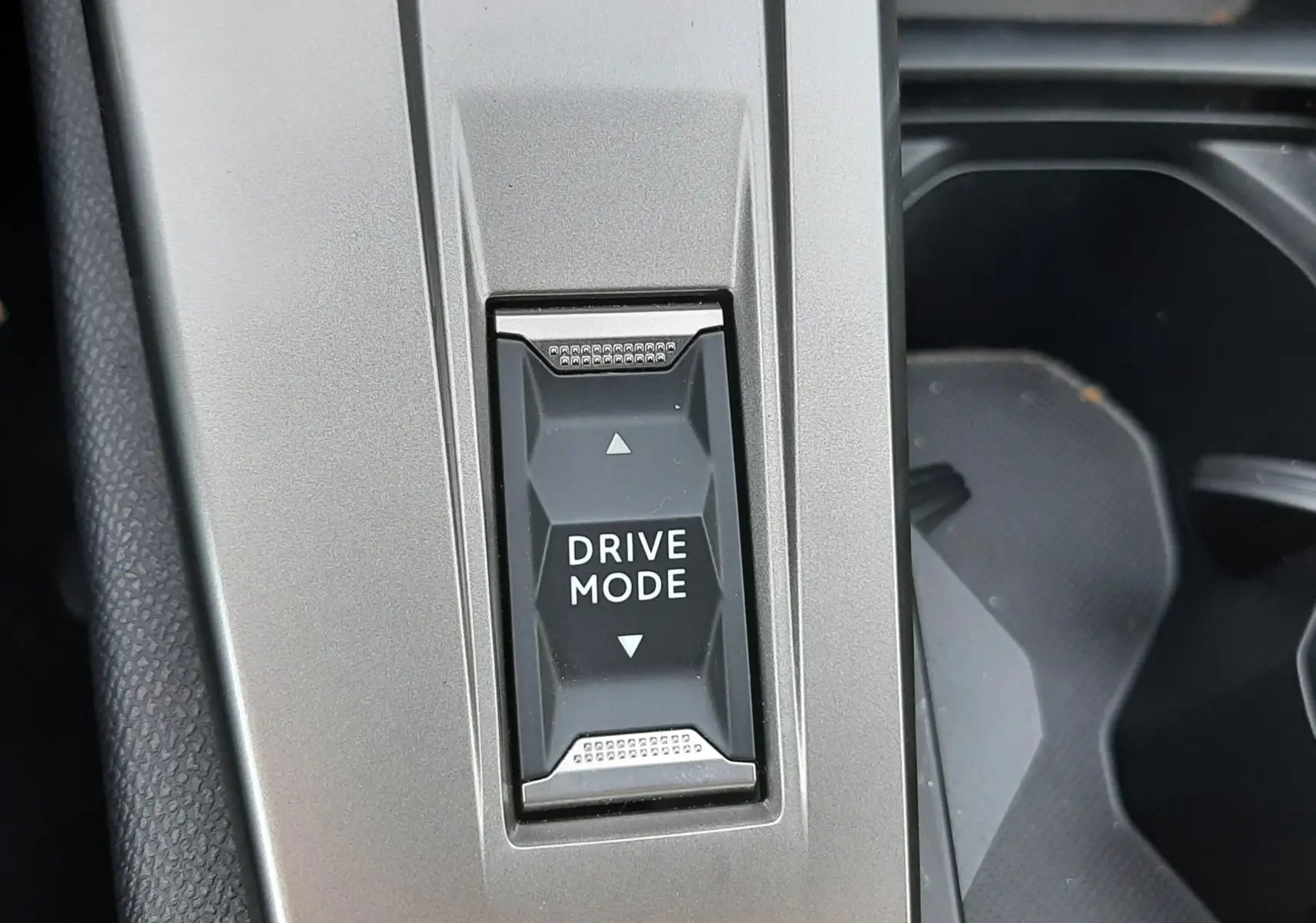 Gros plan sur le bouton Drive Mode intégré dans la console centrale gris sélénium de la Peugeot 408 Hybrid 2024.