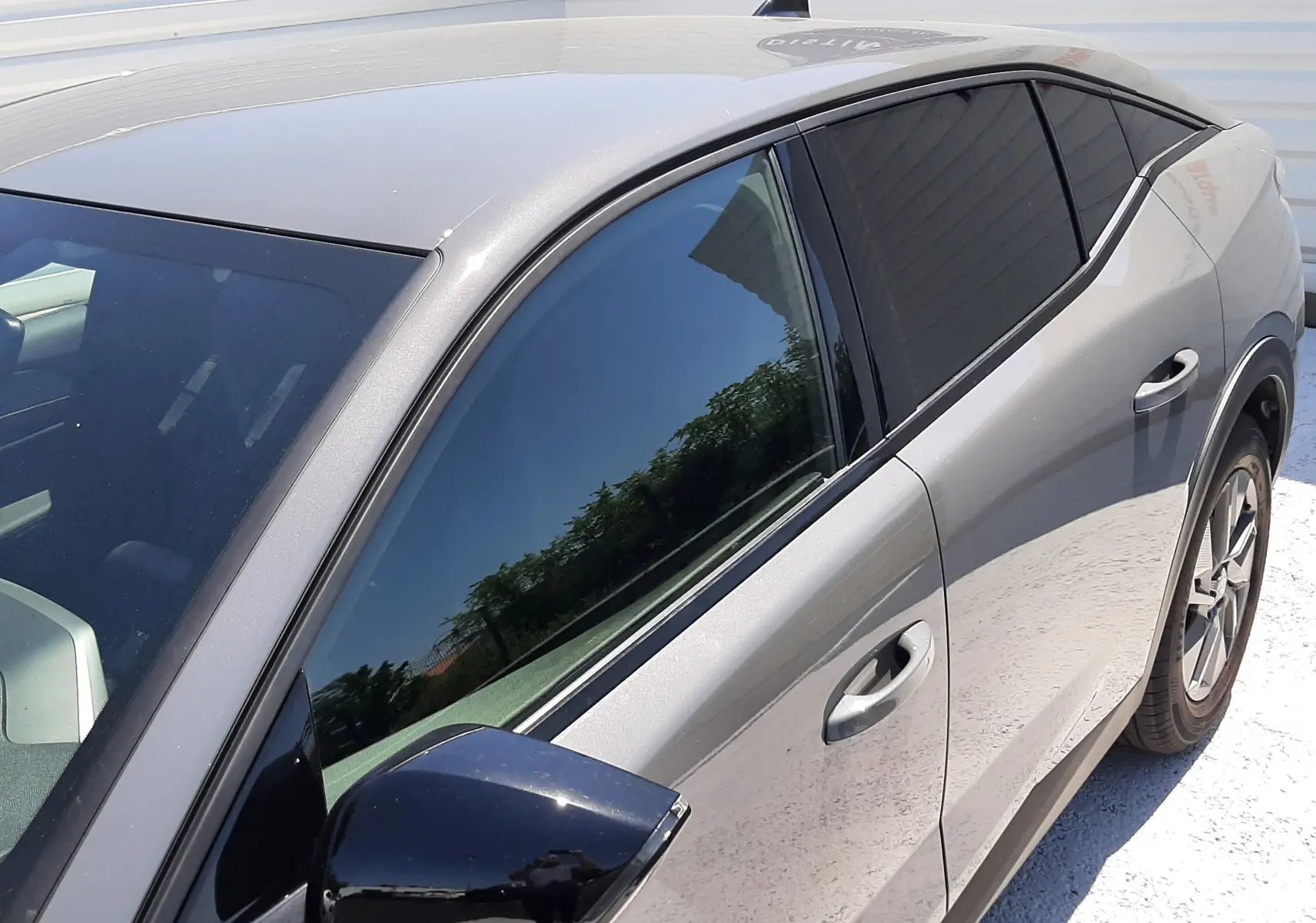 Vue de côté droit avant d'une Peugeot 408 gris selenium avec rétroviseur noir et vitres teintées.