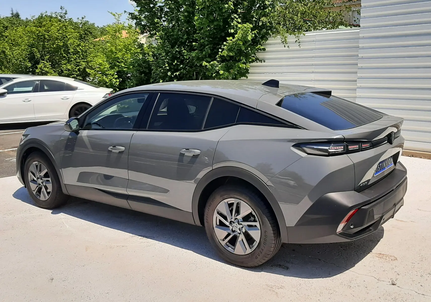 Peugeot 408 Hybrid gris selenium vue 3/4 arrière côté droit, avec toit noir et feux arrière LED distinctifs.