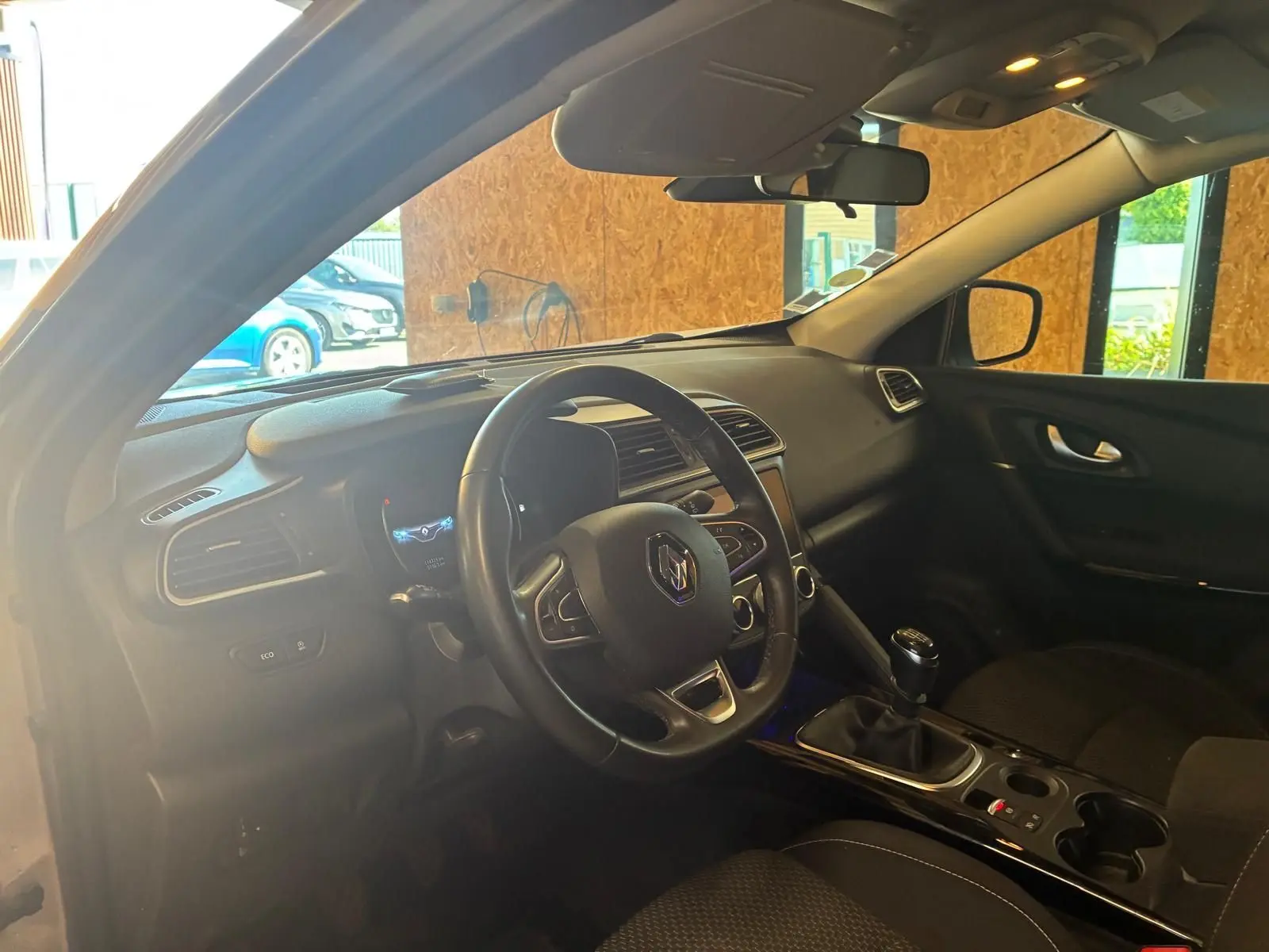 Vue intérieure côté conducteur du Renault Kadjar gris, montrant le volant, la console centrale avec boîte manuelle et tableau de bord.