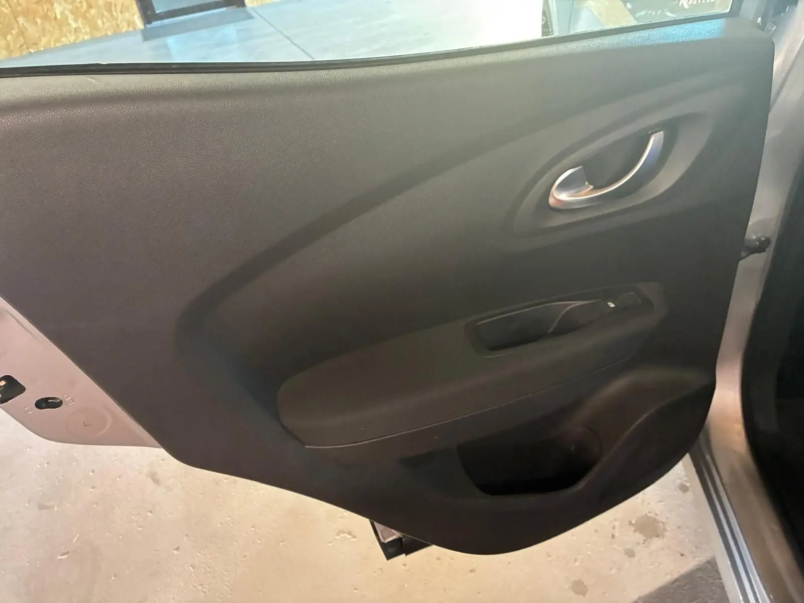 Vue intérieure de la porte arrière droite du Renault Kadjar gris, avec poignée argentée et commande de vitre noire.