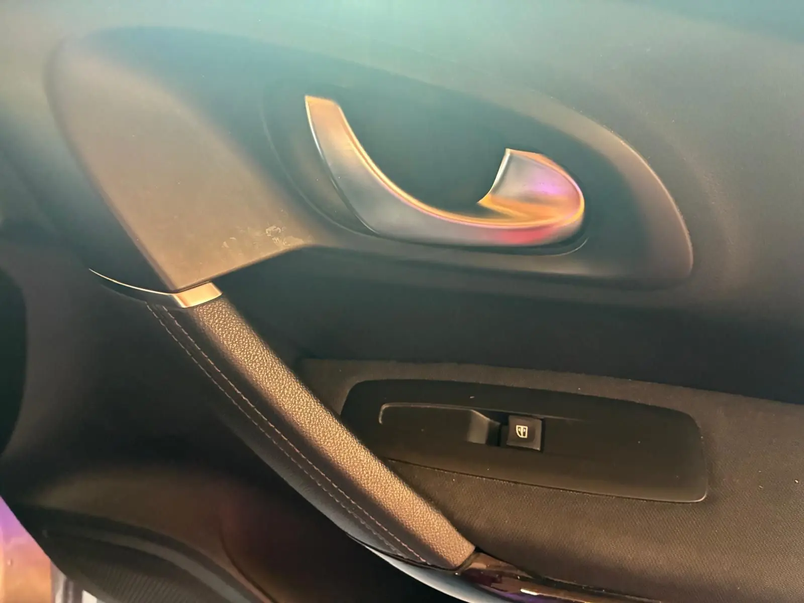 Poignée de porte intérieure côté gauche en métal brossé avec bouton de commande de vitre sur Renault Kadjar gris, vue rapprochée.