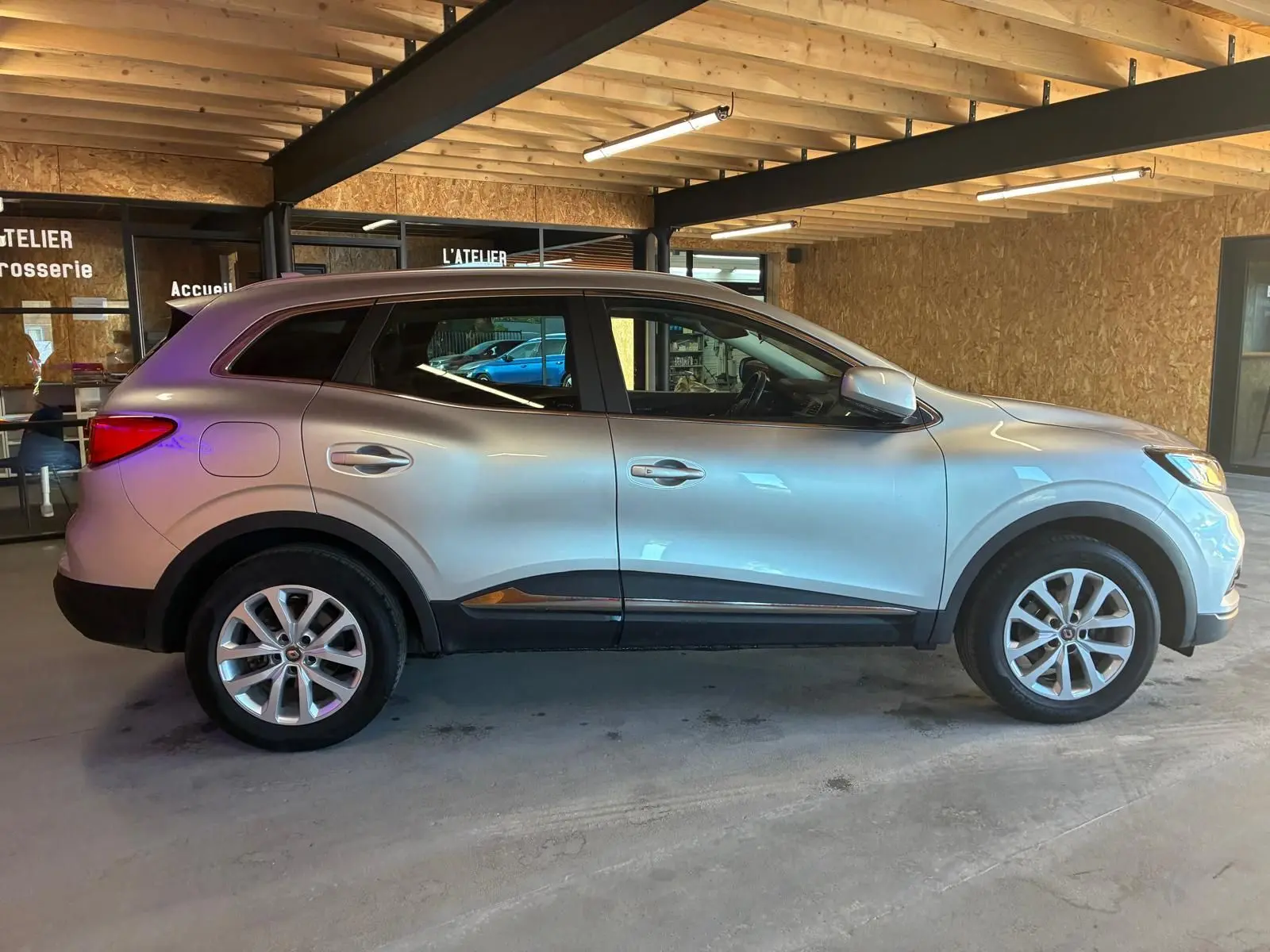 Vue de profil côté gauche d'un Renault Kadjar gris 2020 stationné en intérieur avec jantes alliage visibles.