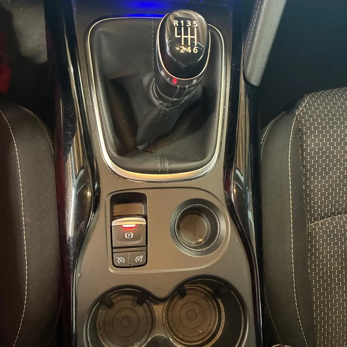 Vue de dessus du levier de vitesses manuel noir et console centrale du Renault Kadjar gris, avec porte-gobelets et bouton frein à main électrique.