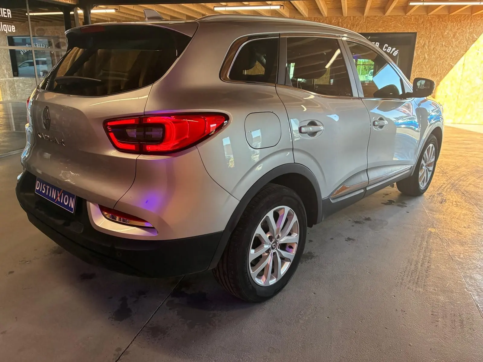 Vue 3/4 arrière droit du Renault Kadjar gris 2020 avec feux arrière allumés dans un garage intérieur.