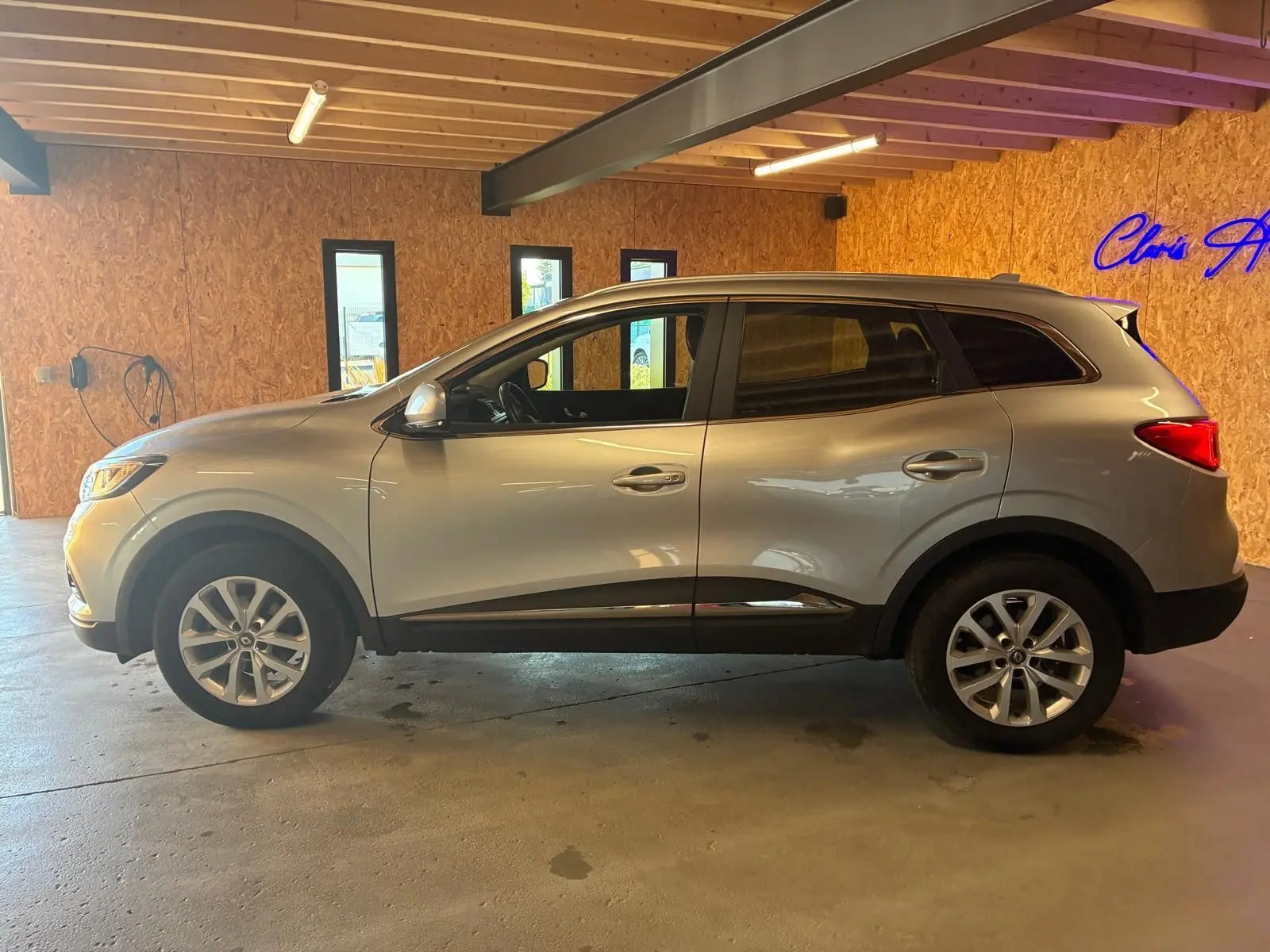 Profil côté gauche d'un Renault Kadjar gris 2020, version 1.5 BlueDCI 115 Business, dans un garage en bois.