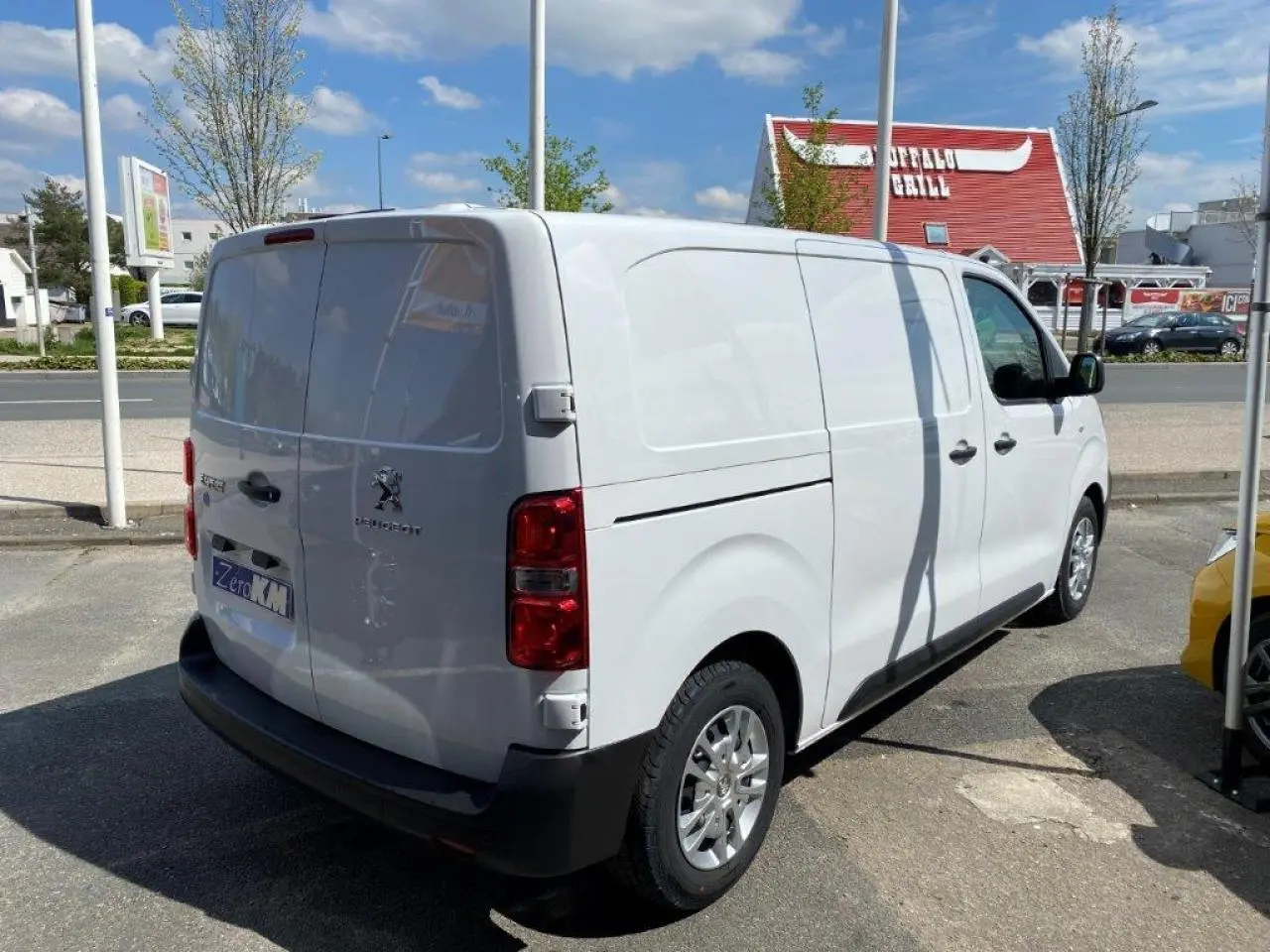 Vue 3/4 arrière droite d'un Peugeot Expert Fourgon blanc stationné en extérieur sous un ciel bleu.