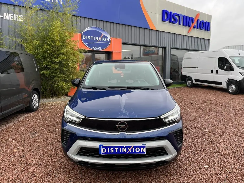 Vue frontale d'un Opel Crossland bleu clair avec toit noir, stationné devant un concessionnaire Distinxion.