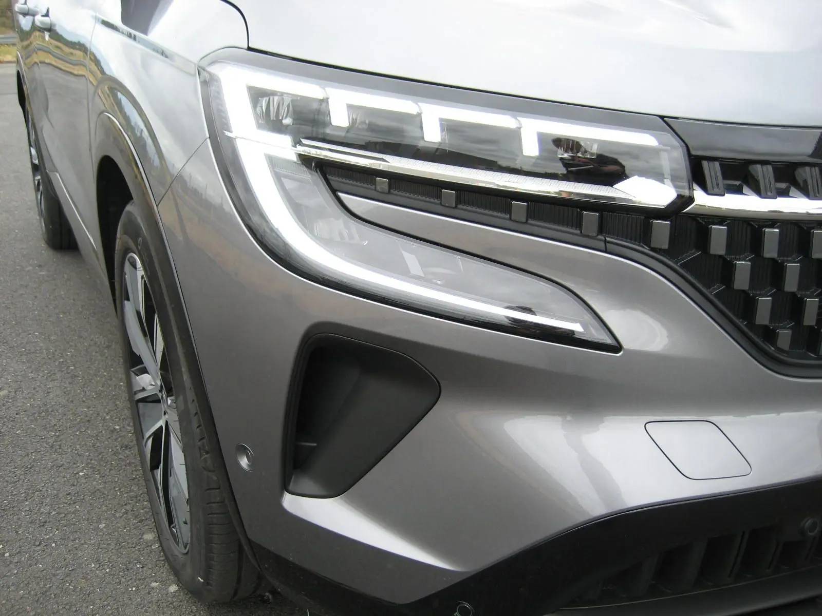 Gros plan sur l'avant gauche du Renault Austral gris 2025, mettant en valeur le phare LED et la calandre moderne.